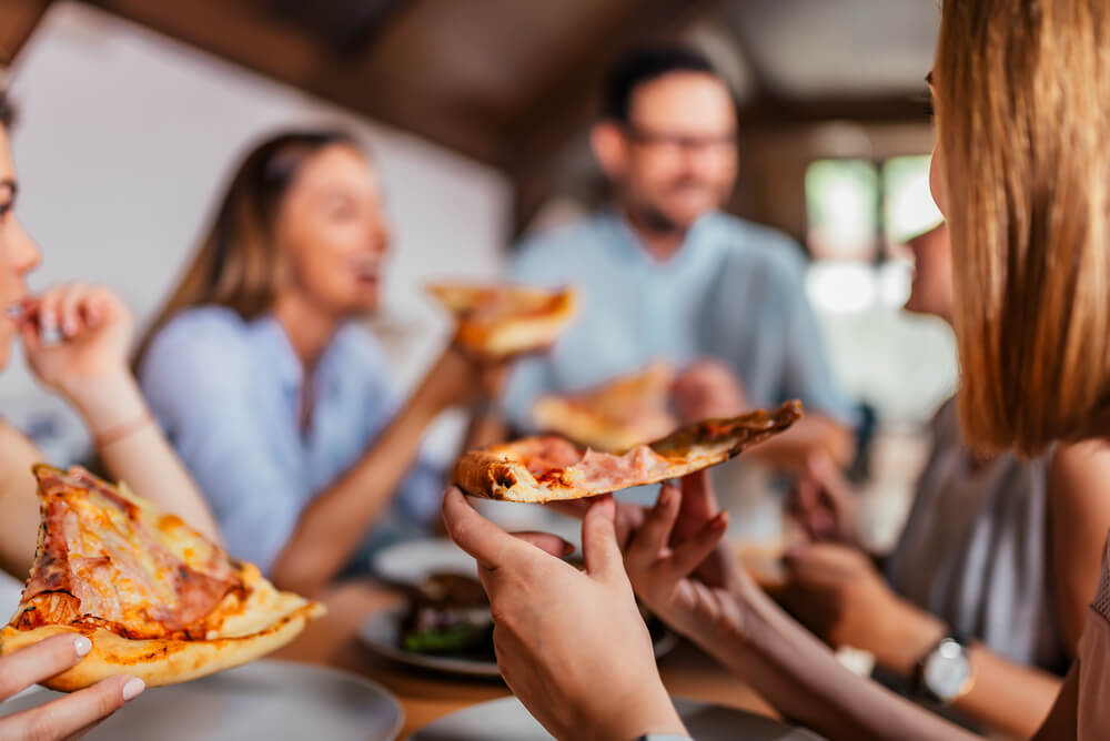 Women eating pizza with man in background
